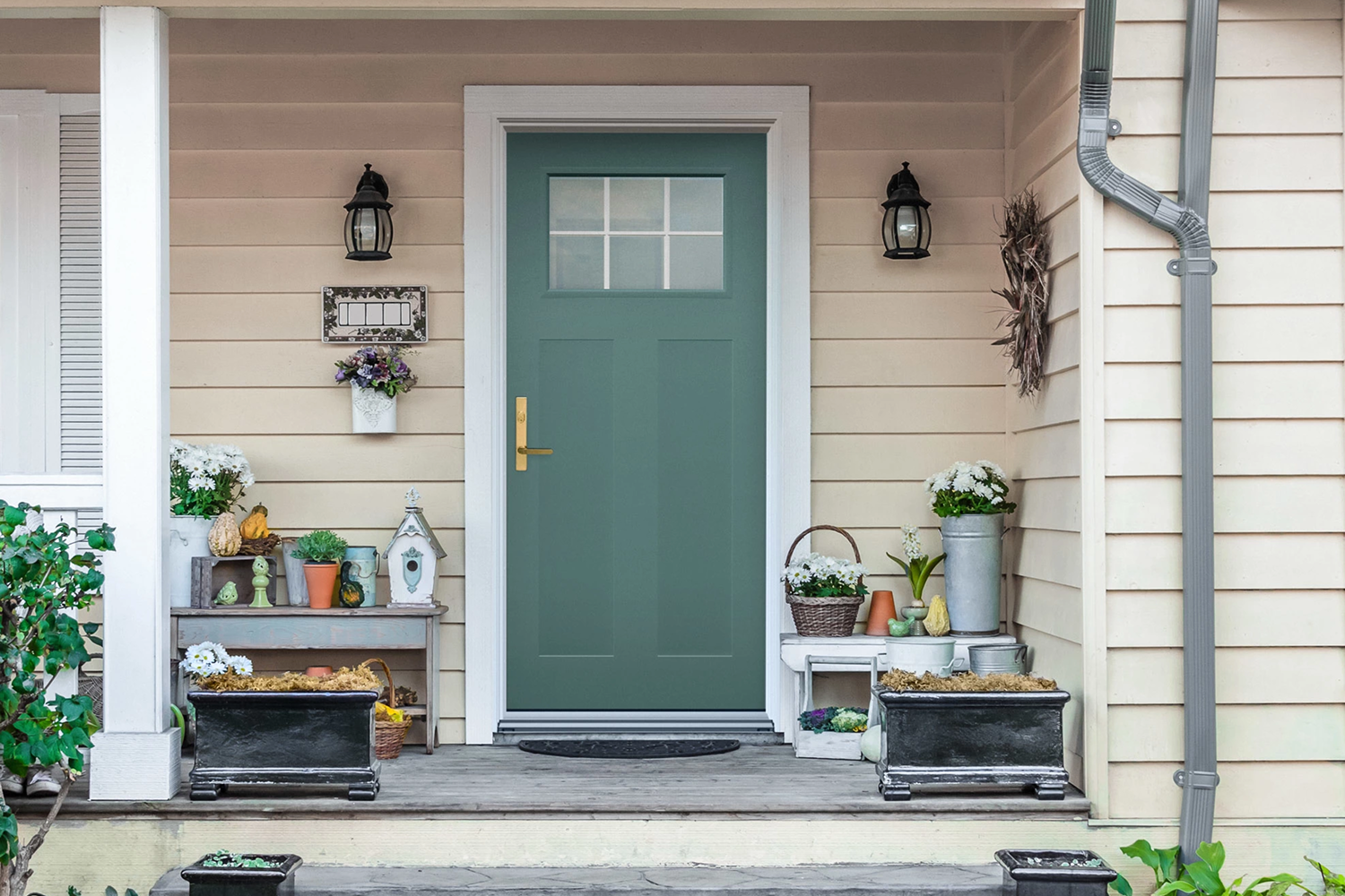 Teal entry door with a small glass panel at the top. The door is frame by white wood and the house has light yellow/tan siding.