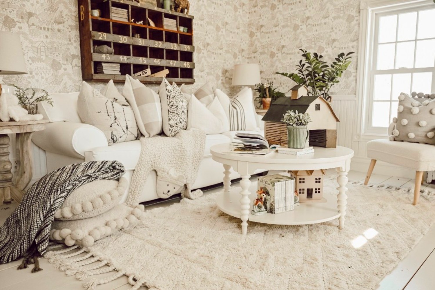 Liz's farmhouse-style sitting room with rustic decor, plush white furniture, a white rug, and light coming in through windows.