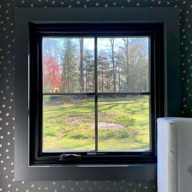 A square casement window with dark green trim and wallpaper.