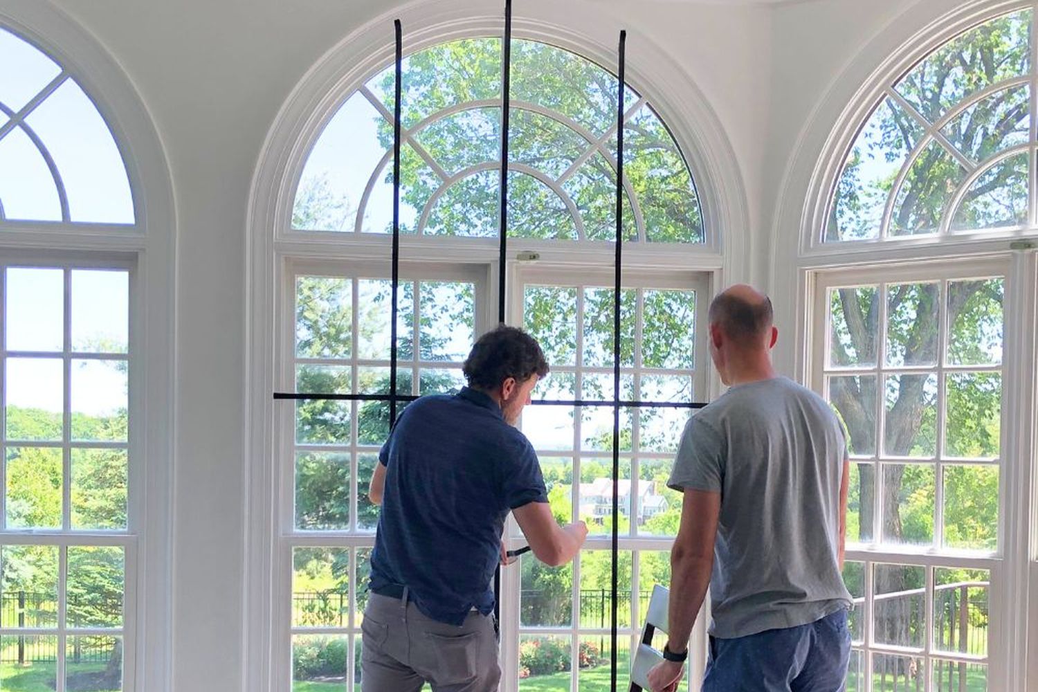 Two men in the mostly remodeled living room holding window grilles.