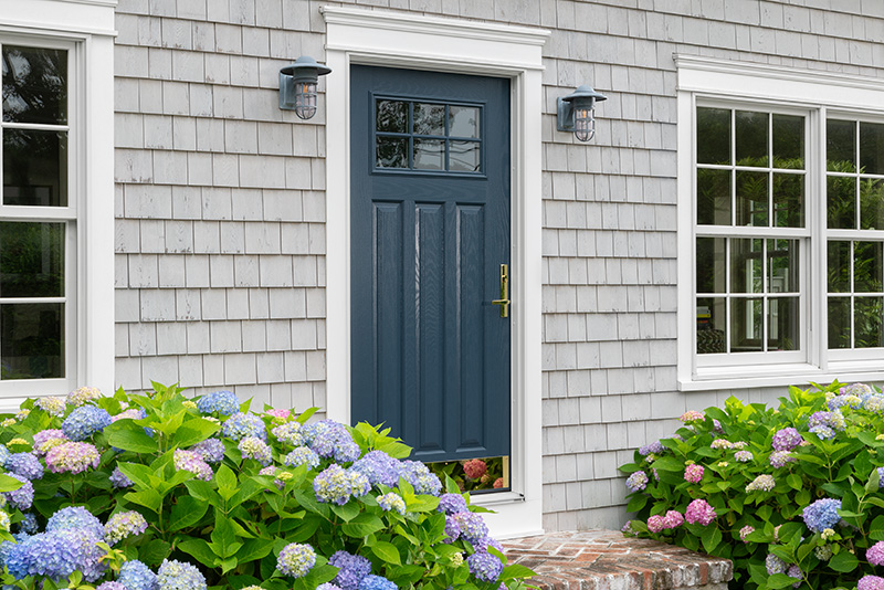 A blue door with white trim, surrounded by colorful flowers in front, creating a welcoming entrance.