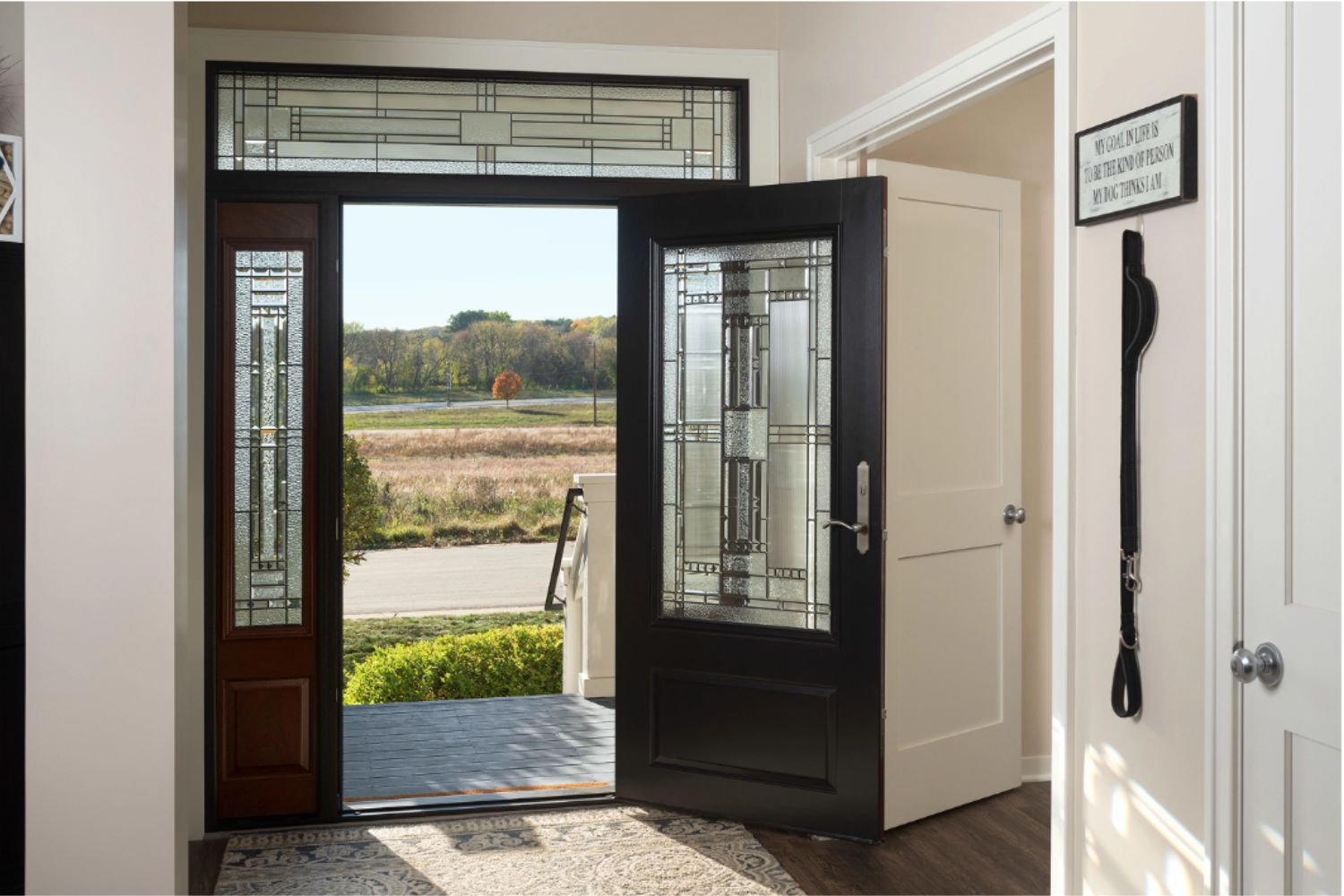 Decorative glass front entry door with matching sidelights and a transom window, opening to a bright foyer with natural light.