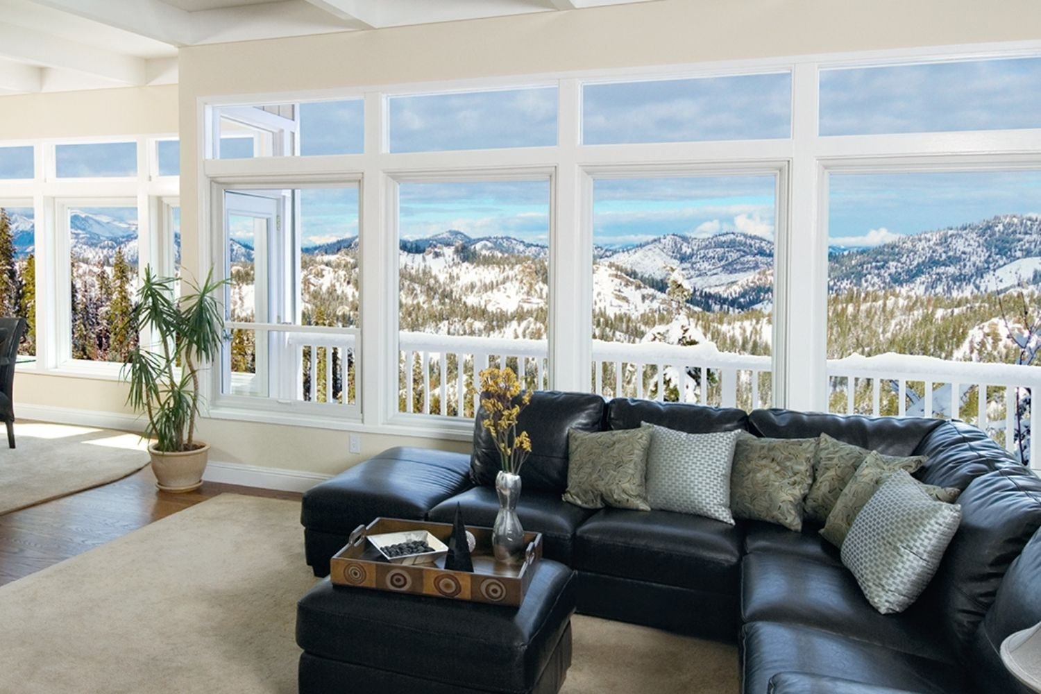 Spacious living room with a black couch and large picture windows all along the exterior wall that let in lots of natural light.