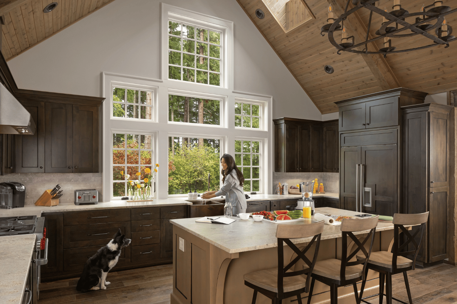 A woman stands in a kitchen, smiling at a dog sitting beside her on the floor.