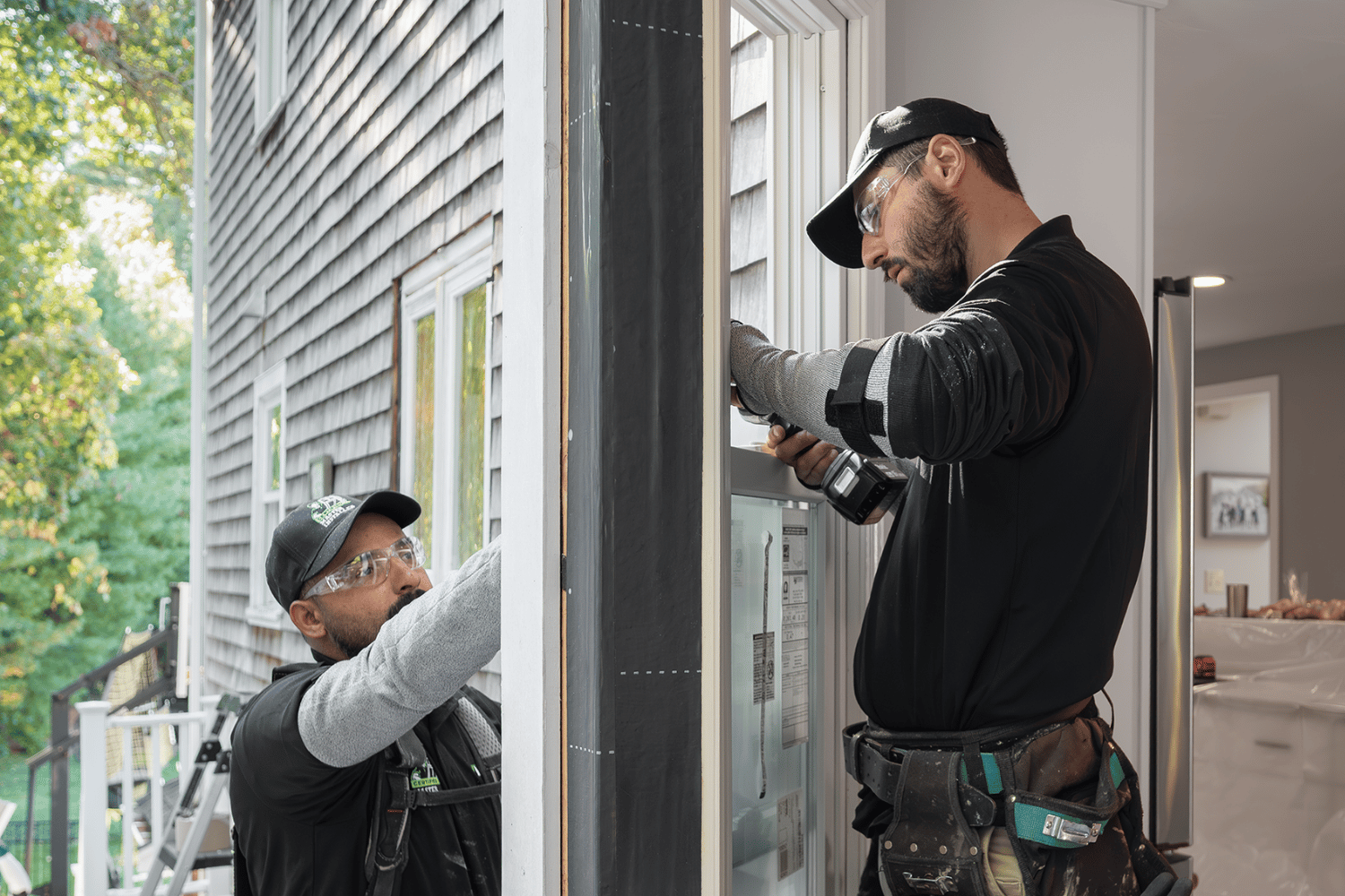Two men installing a window in a house, focused on their task with tools and materials nearby.