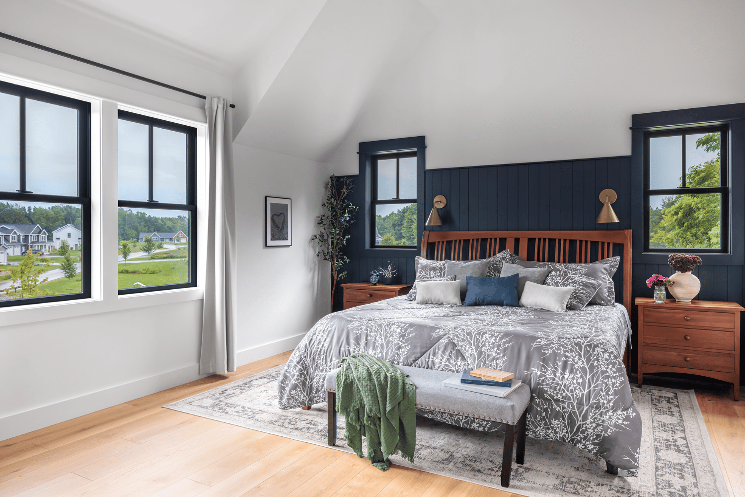 White bedroom with a wood floor and dark blue accent wall with four double hung windows around the room.