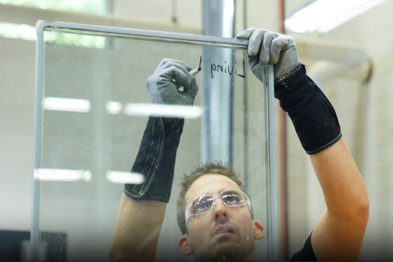 A man in a black shirt and gloves holds a large glass window, preparing for installation or transport.