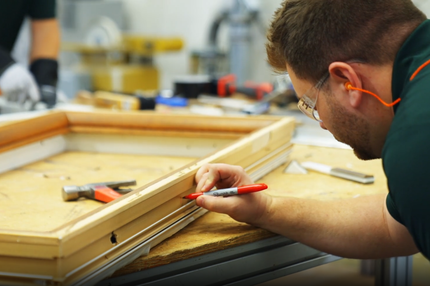 A man constructs a wooden frame in a well-lit workshop, surrounded by tools and materials.