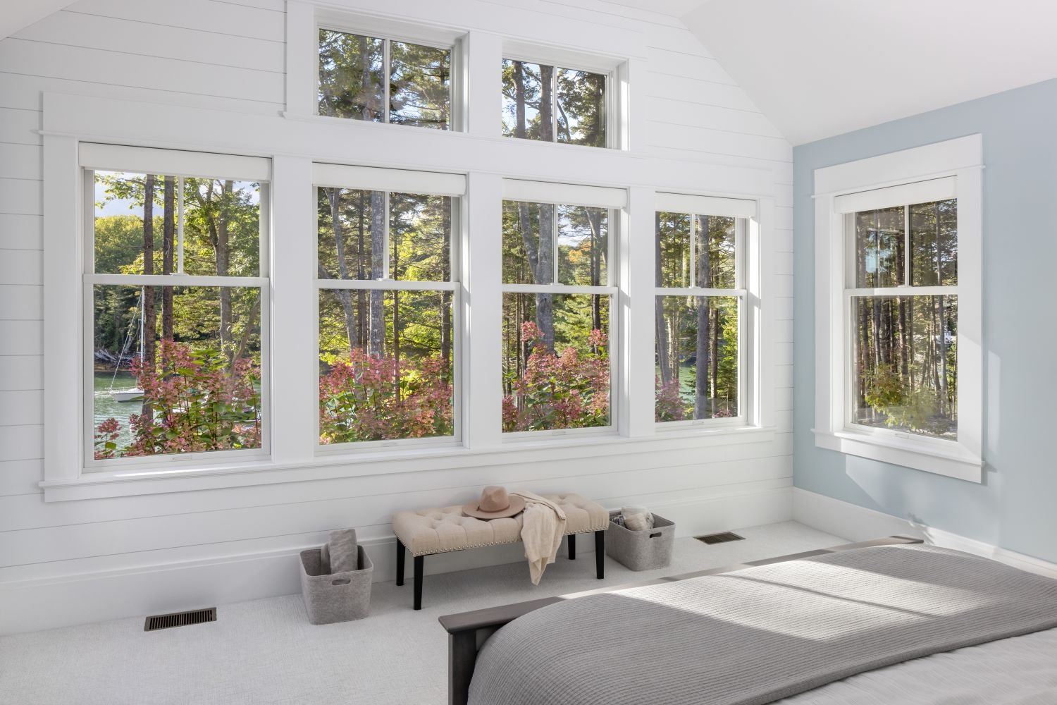 Spacious bedroom with white-framed replacement windows and transom windows, offering abundant natural light and scenic wooded waterfront views. Energy-efficient replacement windows enhance comfort, beauty, and panoramic outdoor visibility.