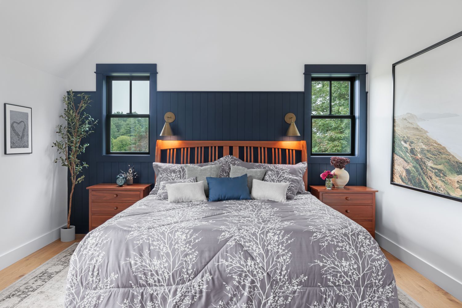 Black-framed replacement windows in a modern bedroom with a navy accent wall, wood furnishings, and abundant natural light. 
