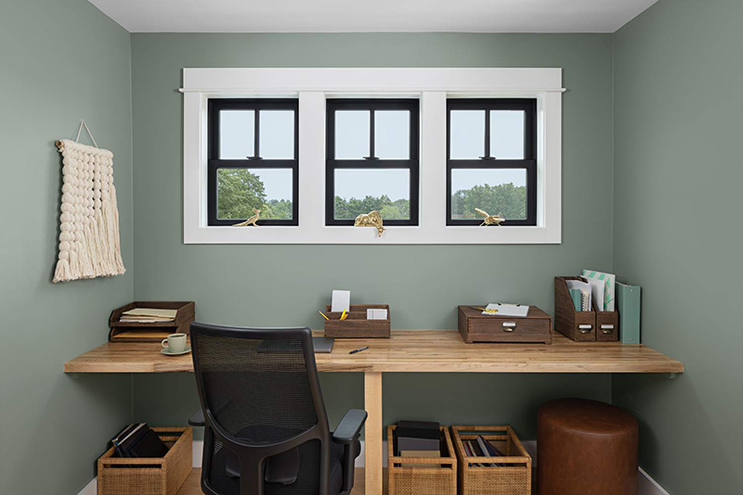 Three black double hung windows side by side within a larger white frame towards the top of the ceiling in a basement office.
