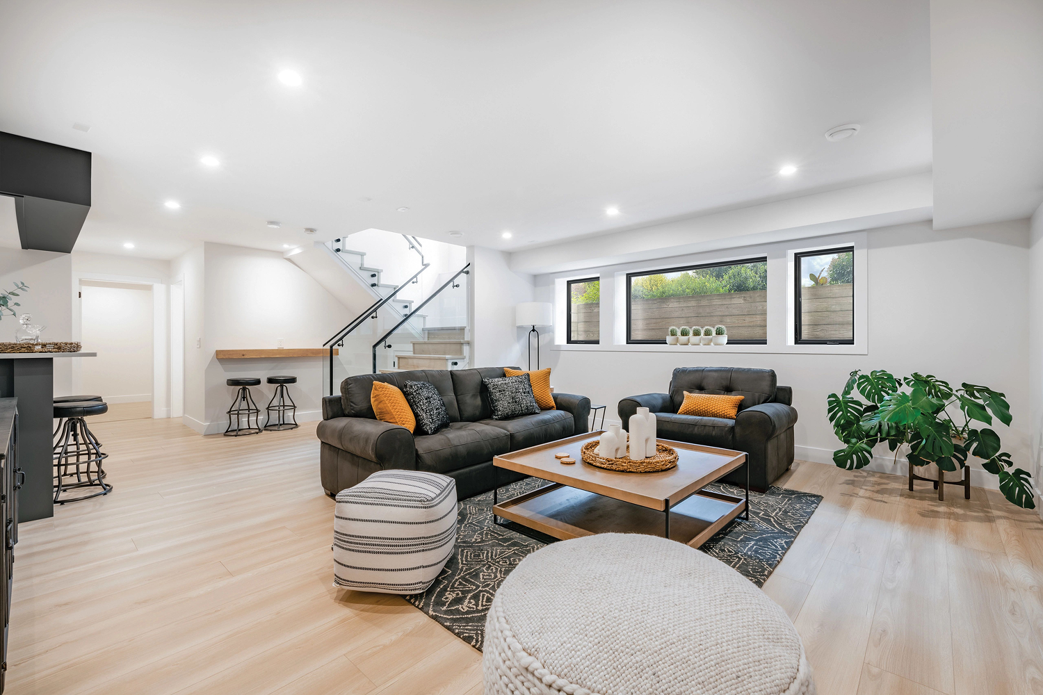 Brightly lit, finished basement with wood floors and white walls. There is a set of windows on the far side of the room.