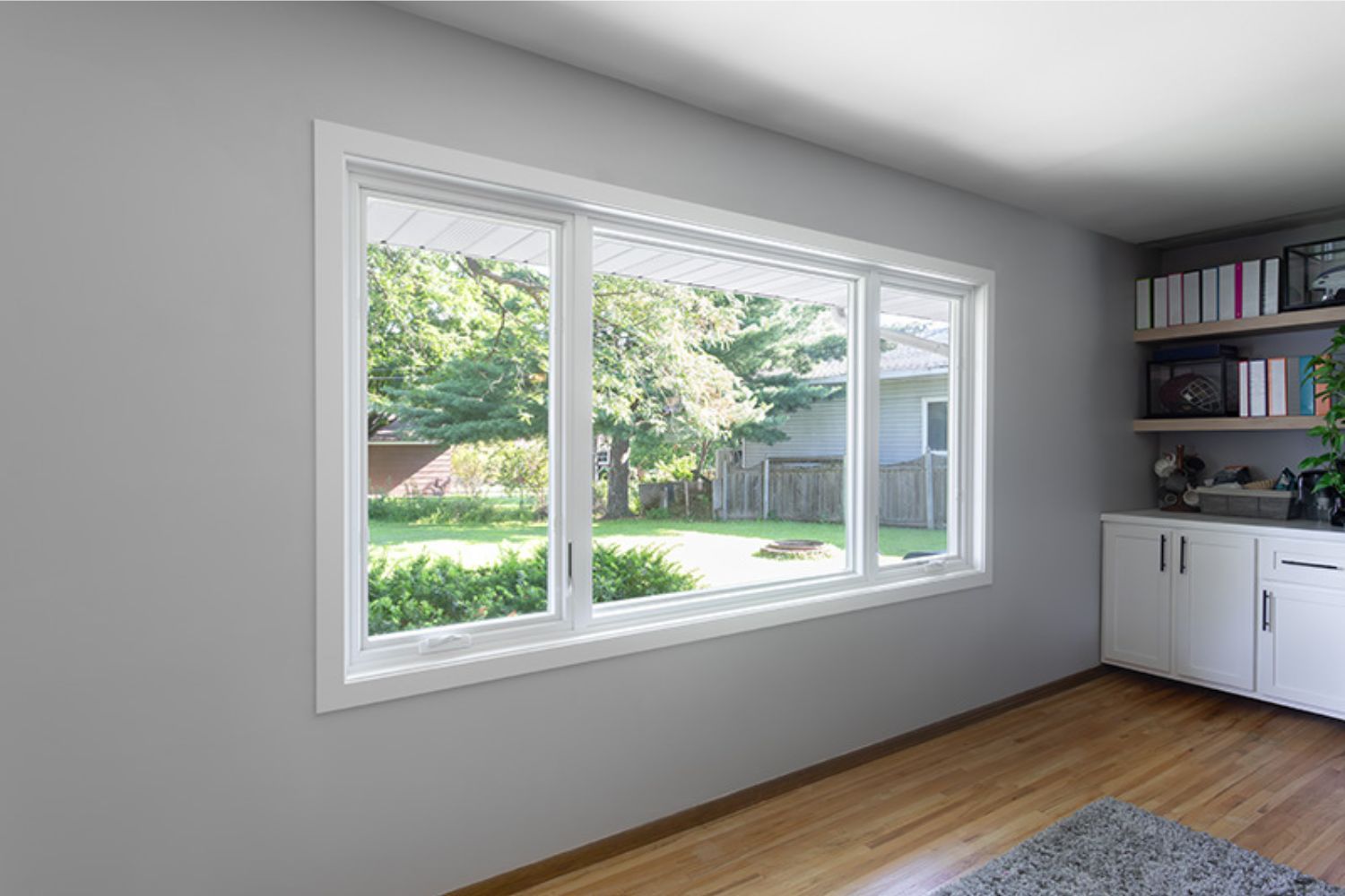 A set of windows with two casement windows on either side of a picture window in the middle with white framing on a gray living room wall. 