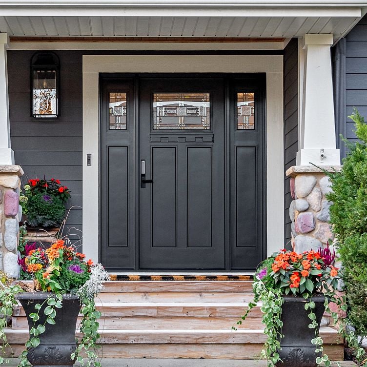 An Ensemble entry door with dual sidelights. The door is black single panel. The sidelights are one third light. There are flower pots in front.