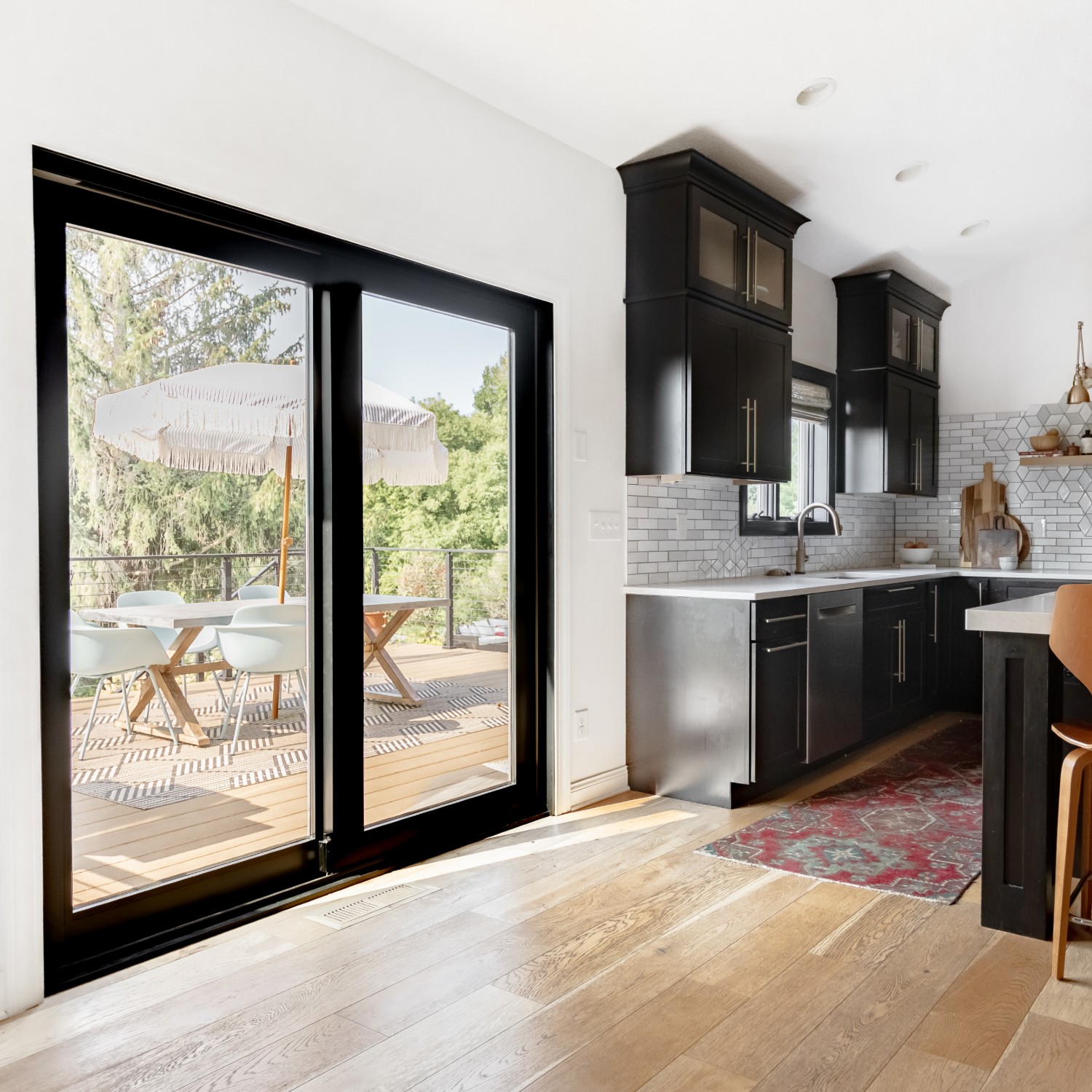 Black contemporary modern sliding glass doors in a kitchen. They look out to a deck and patio table.