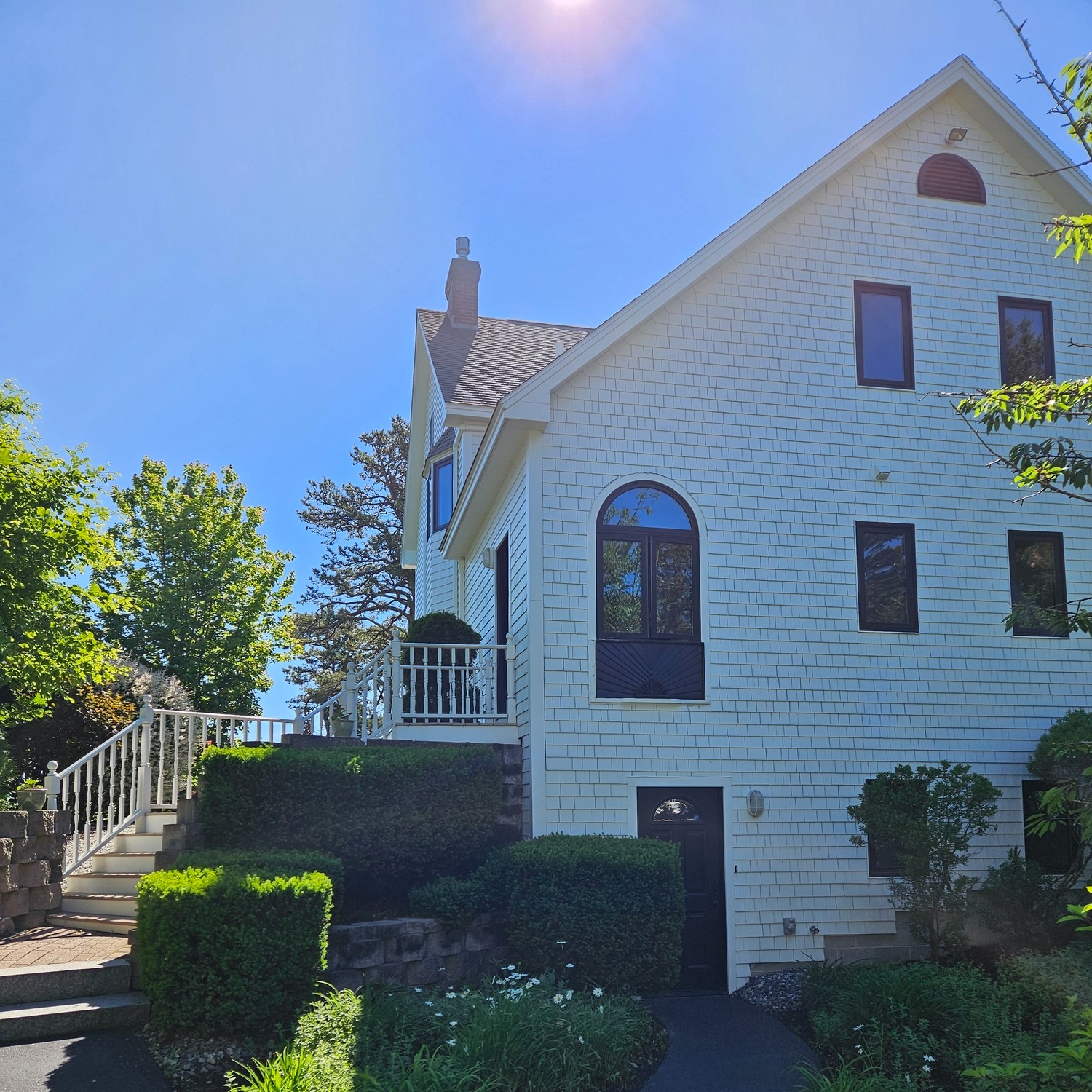 The exterior side of a large white house with black windows. We can see one circle top, one springline, and four double hungs.